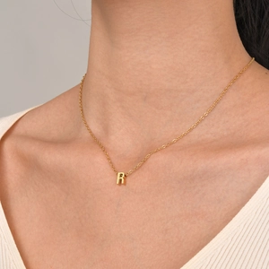 Close-up of a gold-plated letter R pendant on a delicate chain worn by a model
