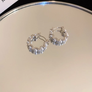 Detailed view of silver hoop earrings with faux pearls and rhinestones on a mirror surface