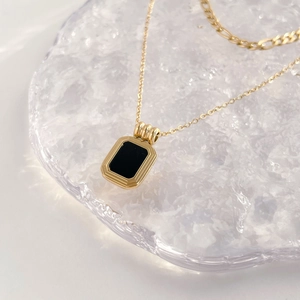 Detailed shot of gold necklace with rectangular black agate pendant on a textured tray