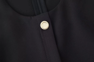 Detail of a decorative gold button and hidden zipper on a black midi dress fabric