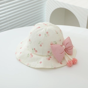Close-up of a white baby sun hat with pink cherry prints and a large decorative bow