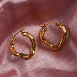 Irregular geometric gold hoop earrings with polished finish on elegant pink silk background