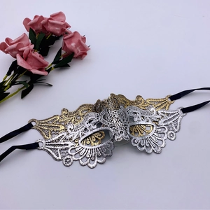 Detailed embroidery view of gold and silver lace eye mask with black satin ribbon ties