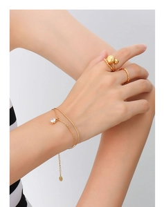Détail du bracelet doré à double chaîne avec zircon scintillant et bagues minimalistes