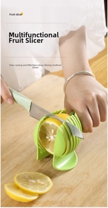 Handheld lemon and tomato slicer tool with green guide slots on a wooden board