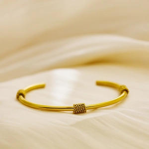Detailed close-up of C-shaped 18k gold-plated bangle with three knot-style accents