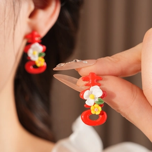 Detailed view of red character earrings with floral accents on a model for a wedding look
