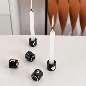 Detail of black ceramic candle holders with white moon patterns and lit candles