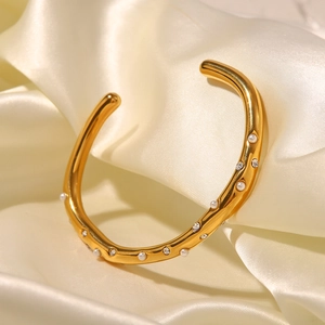 Détail d'un bracelet en titane doré avec perles et zircons sur tissu en soie crème