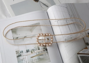 Detail of transparent belt with gold chain trim and pearl-encrusted metal buckle