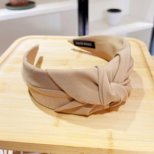 Detail of handmade khaki fabric headband with stylish knot and logo on wooden tray