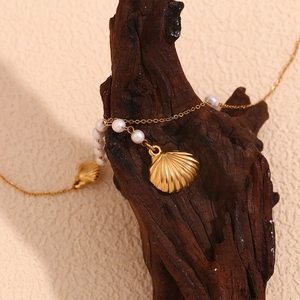 Detail of 18K gold plated seashell pendant with pearl accents on rustic wood backdrop