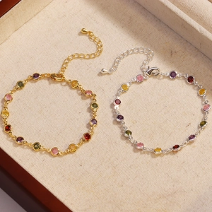 Detailed view of gold and silver bracelets featuring colorful gemstones on beige fabric