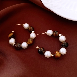 Close-up of tiger eye and pearl hoop earrings on dark red velvet with 16K gold plating