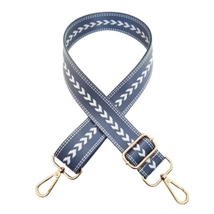 Macro detail of blue embroidered nylon bag strap with gold lobster clasps and buckle