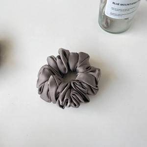 Elegant grey satin oversized scrunchie with French ruffles and silky texture on white surface