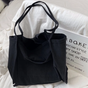 Detail of a large black canvas tote bag with front pocket and durable dual shoulder straps