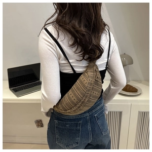 Detail of a large brown woven crossbody bag with a crescent shape and textured finish