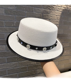 Detail of white boater straw hat with black leather strap and pearl flower accents