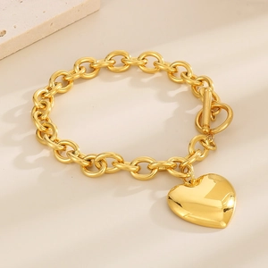 Detailed view of a gold heart pendant bracelet with a toggle clasp on a textured surface