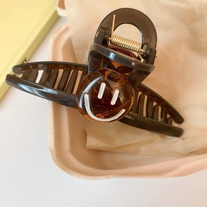 Détail d'une pince à cheveux en acétate marron avec smiley blanc dans un décor raffiné