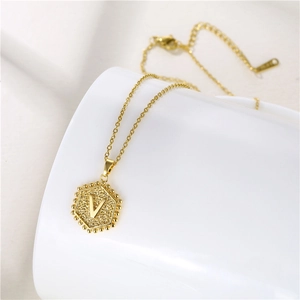 Detailed view of golden hexagonal letter V pendant necklace on a ceramic edge