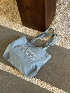 Blue denim tote bag with Less Mondays More Sundays embroidery on stone background