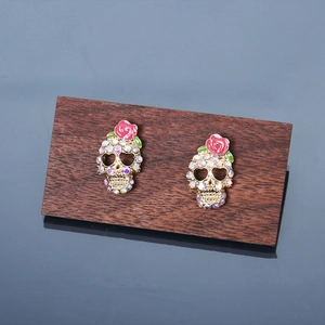 Punk style skull and red rose stud earrings with colorful rhinestones on a wooden stand