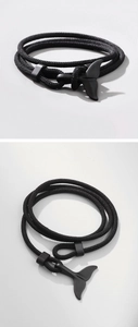 Close-up of a black woven rope bracelet featuring a matte black whale tail charm