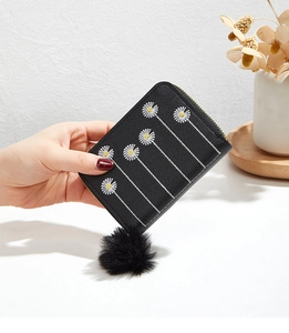 Close-up of black PU leather wallet with daisy embroidery, gold zipper, and pompom charm