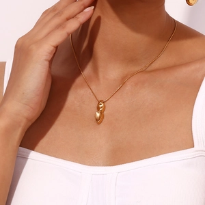 Détail d'un pendentif cacahuète doré sur une chaîne serpent porté par un mannequin