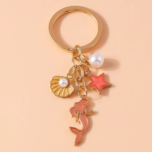 Detail of golden mermaid keychain with pearl, shell, and starfish charms on pink background