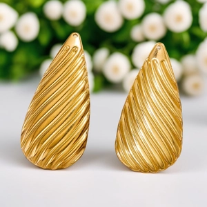 Golden teardrop earrings with textured diagonal stripes on elegant white floral background