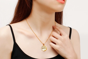 Close-up of golden tree of life pendant necklace worn by a model on white background