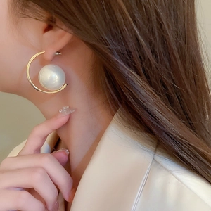 Detail shot of a minimalist gold C-shaped earring with a large round white pearl on a model