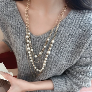 Close-up of elegant multilayer faux pearl necklace worn over a grey autumn sweater