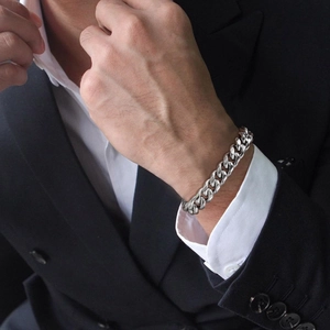 Close-up of a silver cuban link chain bracelet on a male wrist with suit detail
