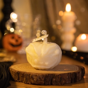 White Halloween Jack-O-Lantern scented candle on a rustic wood slice with festive bokeh