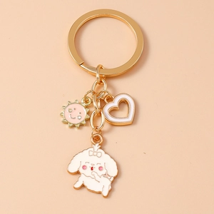 Detail of golden keychain with white enamel poodle, sun, and heart charms on light background