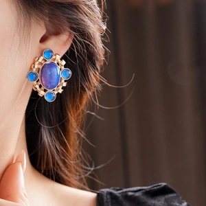 Detail of vintage gold rhombic earring with dark blue gems worn by a female model