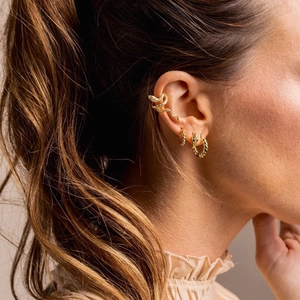 Detail of a golden snake-shaped ear cuff and earring set on a model ear