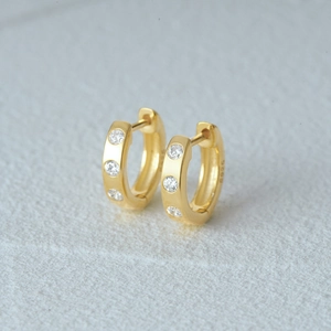 Macro detail of gold plated 925 silver hoop earrings with three inset round zircons