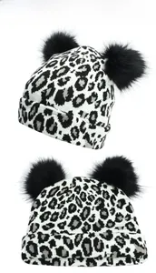 Detail of leopard print knitted hat featuring two fluffy black faux fur pom poms