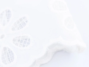 Close-up of white water-soluble lace fabric with floral embroidery and scalloped edges