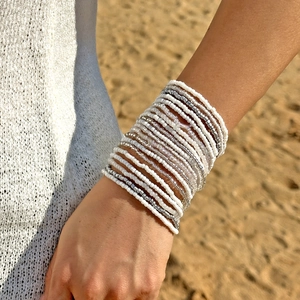 Gelaagde witte en zilveren kralenarmbanden om de pols met een zonnige strandachtergrond