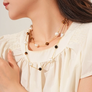 Detail of layered gold necklace featuring baroque pearls and tiger eye stone beads on a model