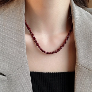 Close-up of a deep red crushed stone beaded necklace worn with a khaki herringbone blazer