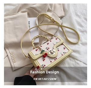 Close-up of yellow crossbody bag featuring red cherry prints and floral metal clasp
