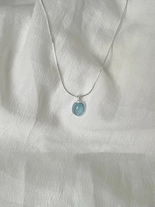 Detail of an oval light blue aquamarine pendant on a slender silver chain necklace