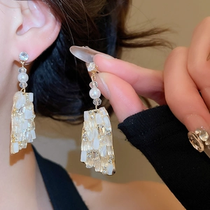 Detailed view of long gold drop earrings with pearls and faceted crystals on a model